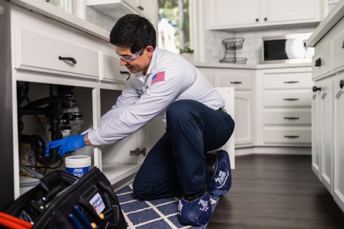 Diego from Benjamin Franklin Plumbing working under a sink in a kitchen
