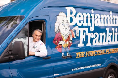 Benjamin Franklin plumber smiling while looking out the driver side of his service van